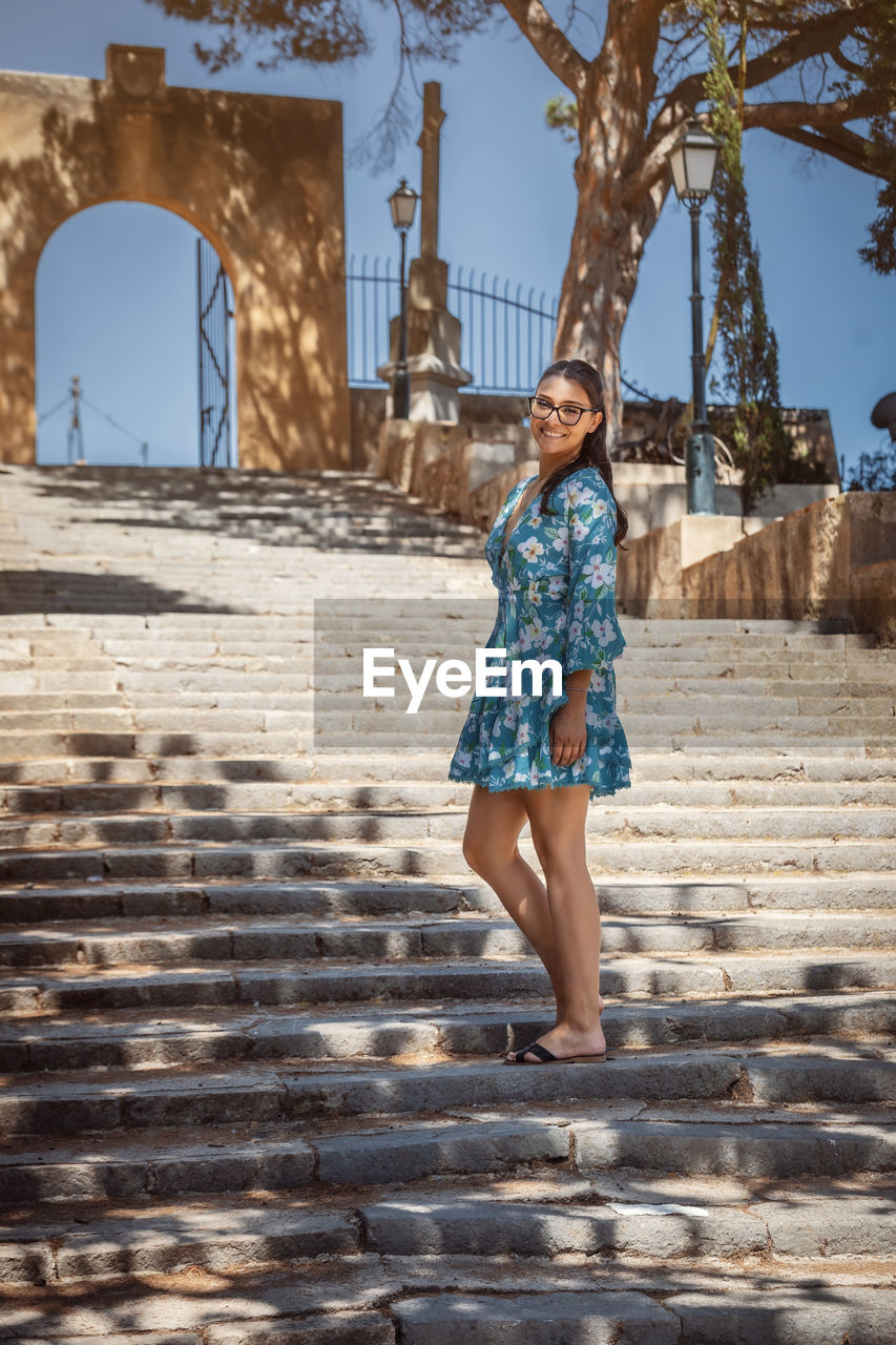 Young woman in summer dress and glasses standing on a staircase