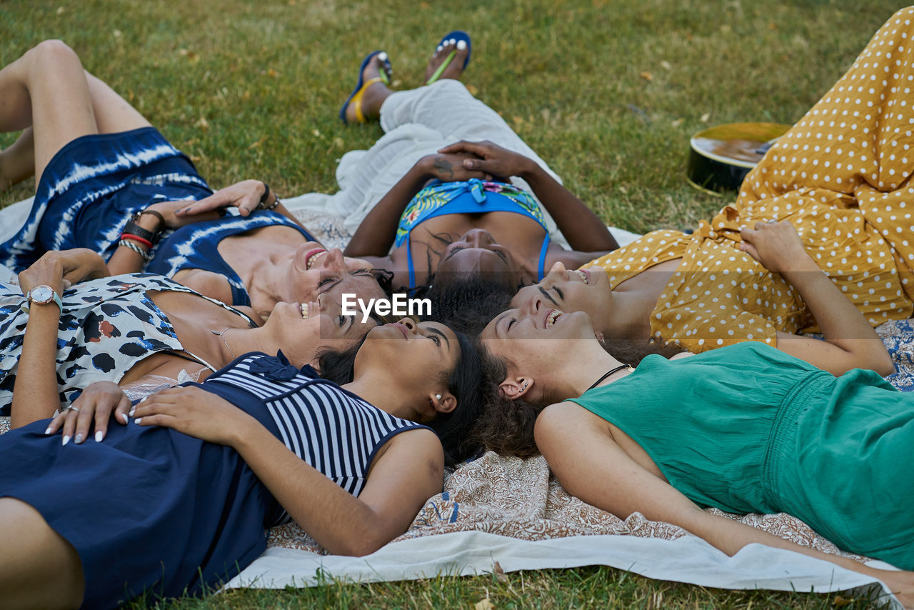 Group of smiling female friends laying on a towel in a park having fun