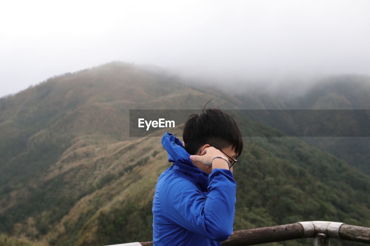 Side view of man wearing warm clothing against mountains during foggy weather