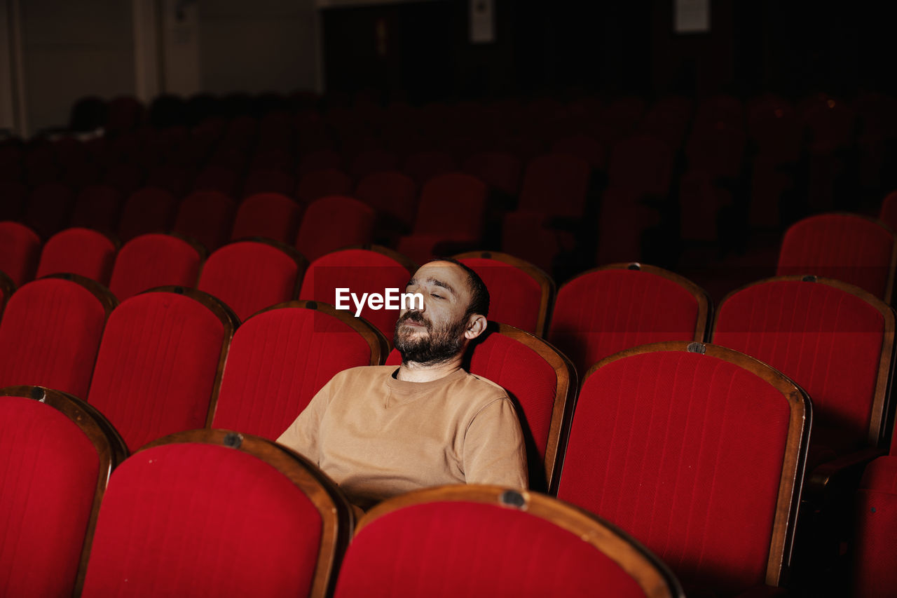 Man looking away while sitting on chair in theater