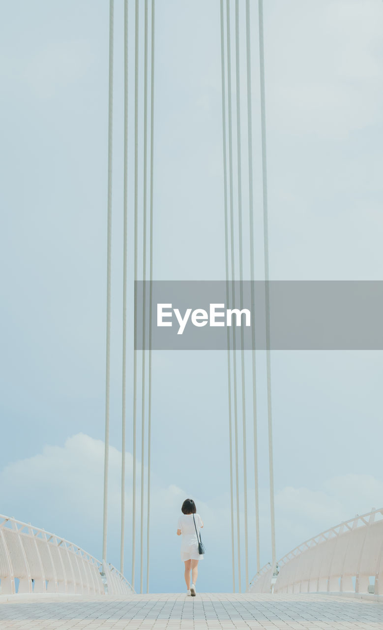 Rear view of woman walking on bridge against sky