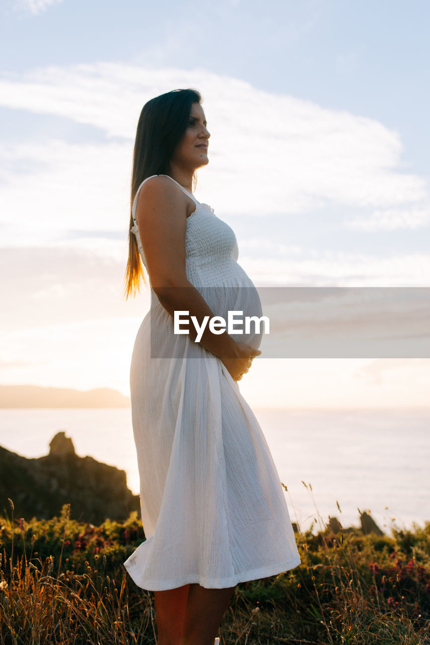 Pregnant woman standing on field by sea against sky