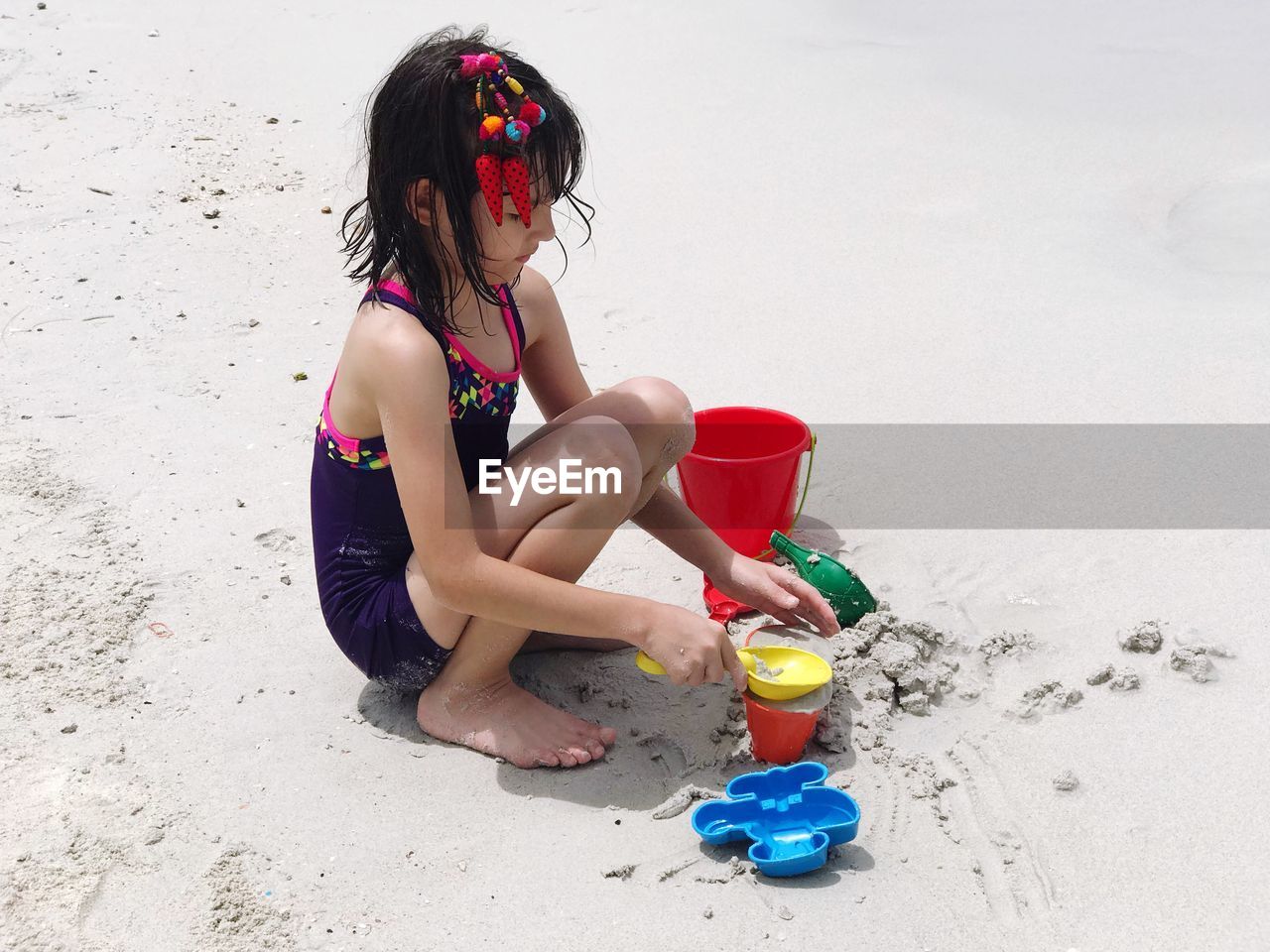 Girl playing with toys while crouching on sand at beach
