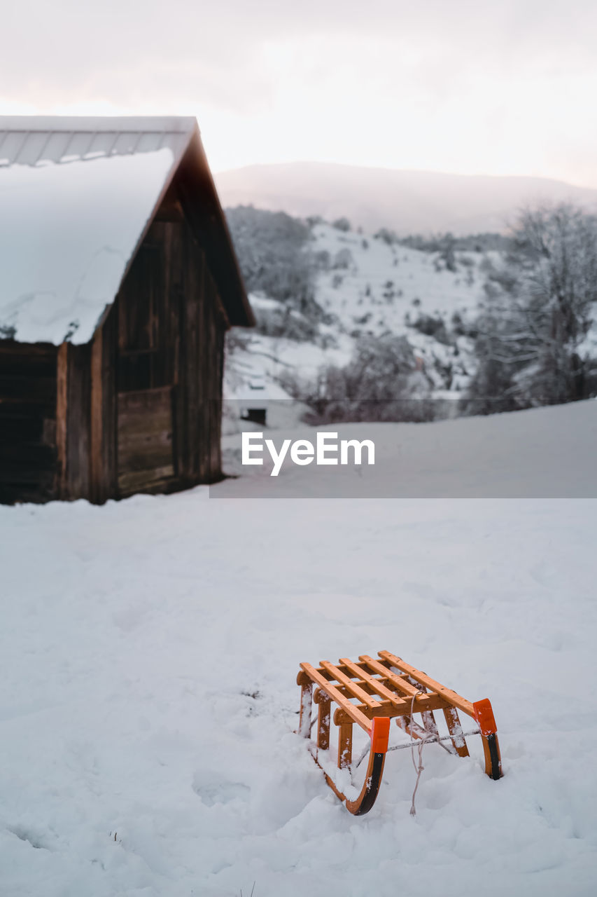 Snow on field against clear sky with wood sledge in front of a cabin during winter