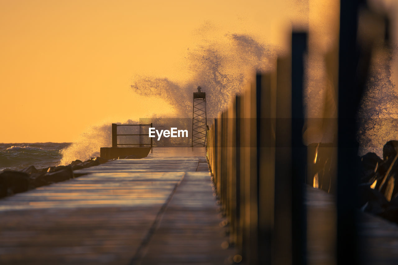 Pier in nørre vorupør during sundown with a big wave splashing against it
