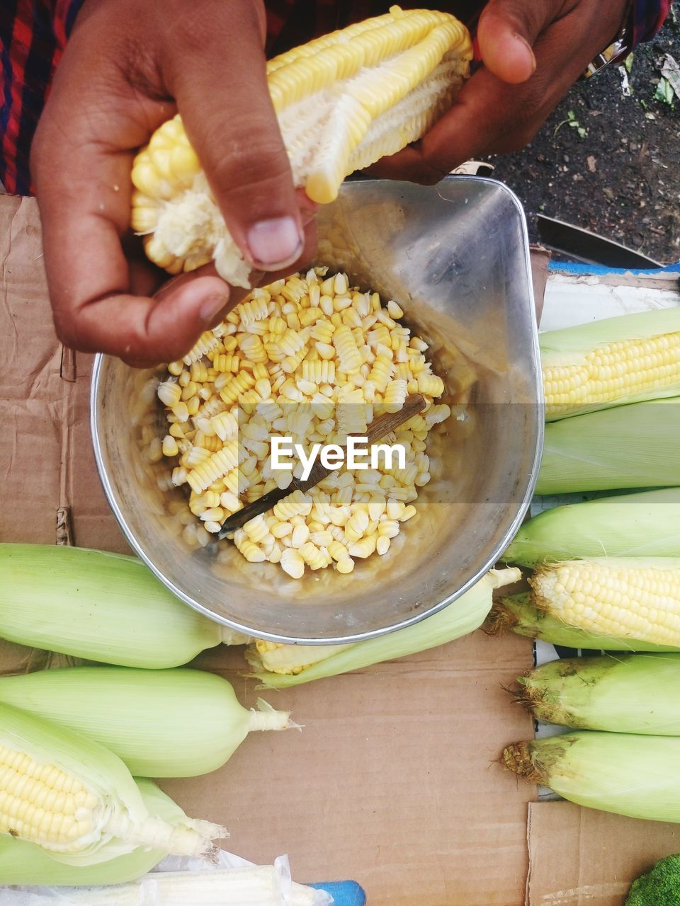Cropped image of vendor holding corn over container