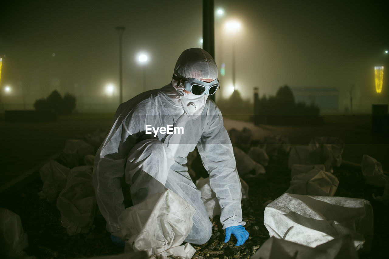 Full length of man wearing protective suit crouching outdoors at night