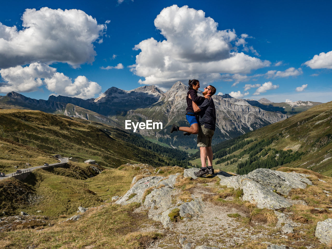 Side view of boyfriend carrying girlfriend while standing on mountain against sky