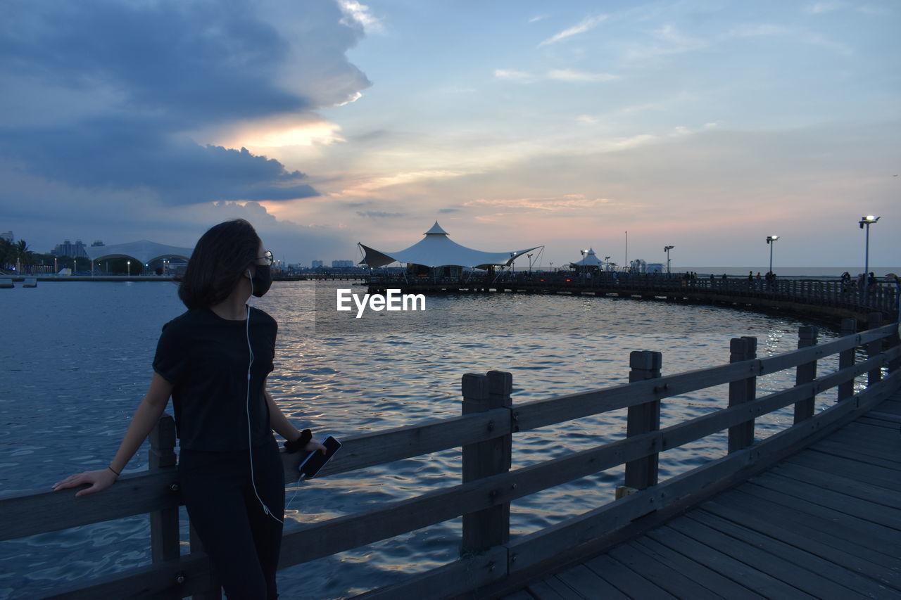 Girl standing on pier over sea against sky during sunset