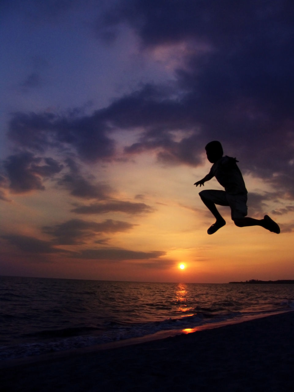 Silhouette of boy jumping by sea