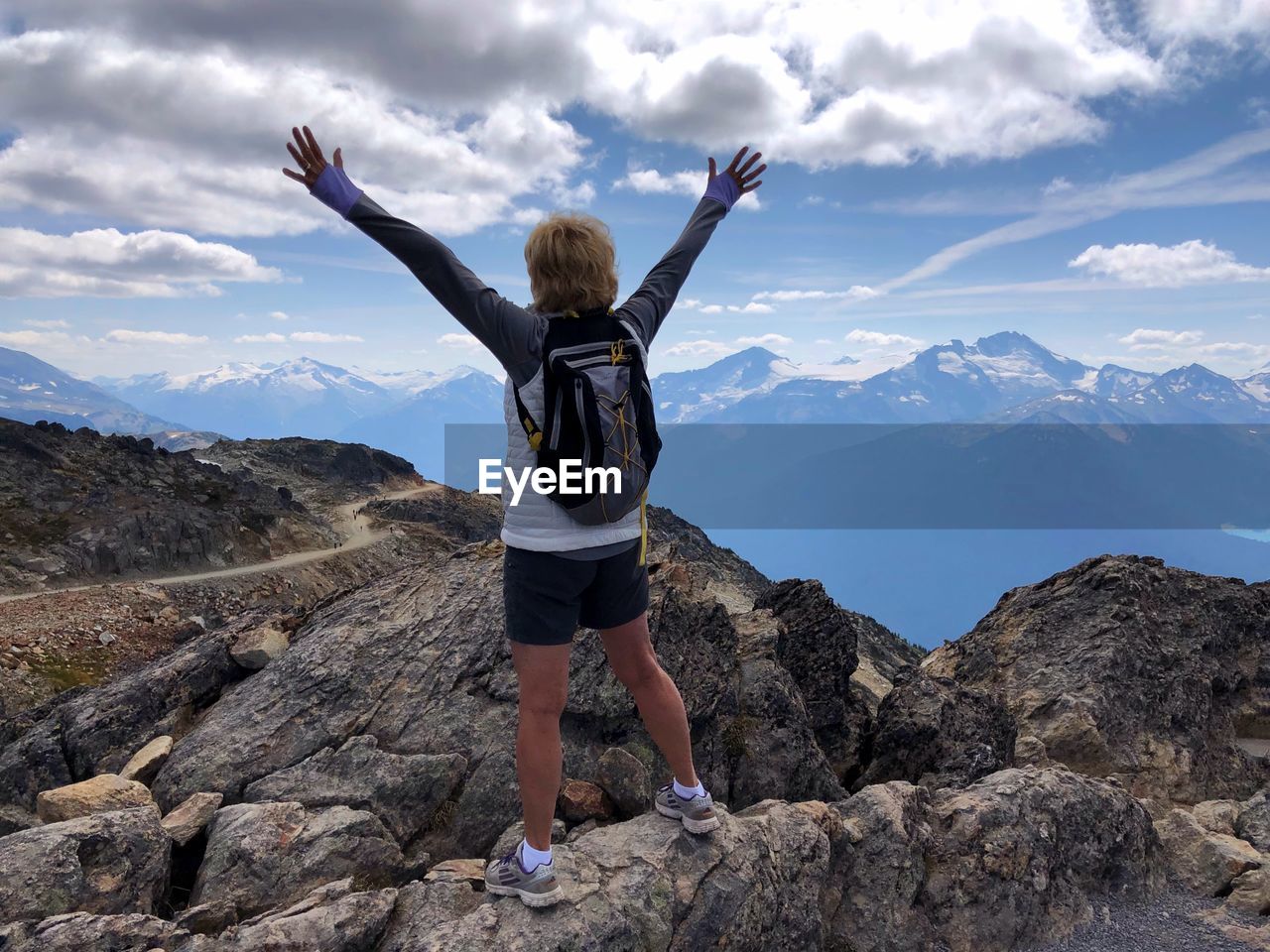 Rear view of woman with arms raised standing on mountain against sky