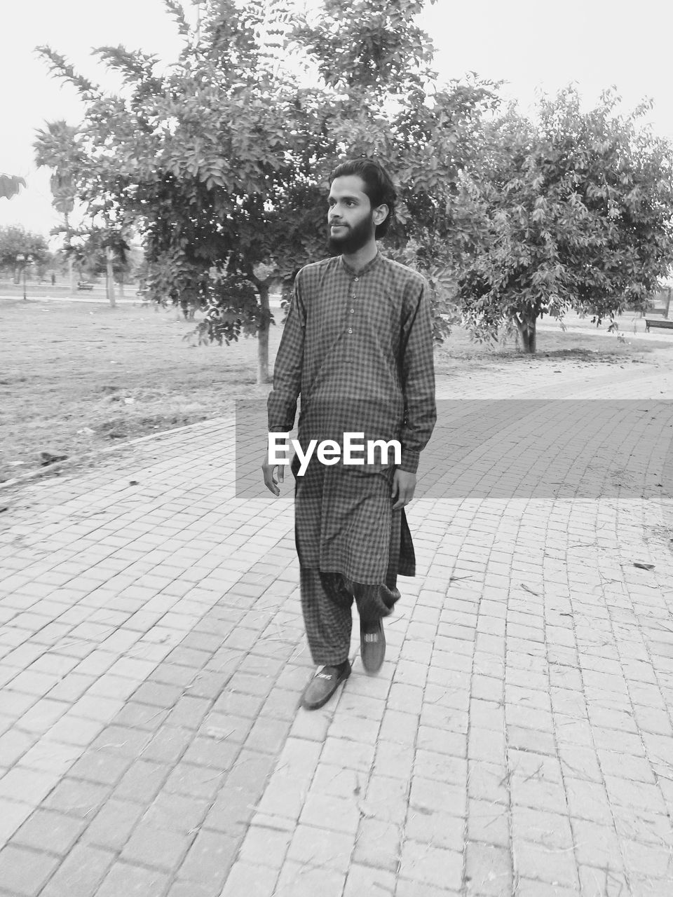 one person, full length, black and white, footpath, tree, adult, monochrome photography, plant, lifestyles, front view, day, monochrome, young adult, men, nature, casual clothing, walking, leisure activity, clothing, portrait, white, looking at camera, spring, outdoors, footwear, city, fashion, standing, street, person, black, sky