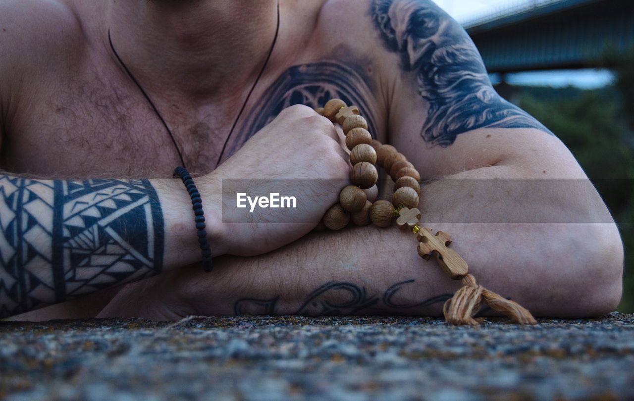 Midsection of man with tattoos on body holding rosary beads