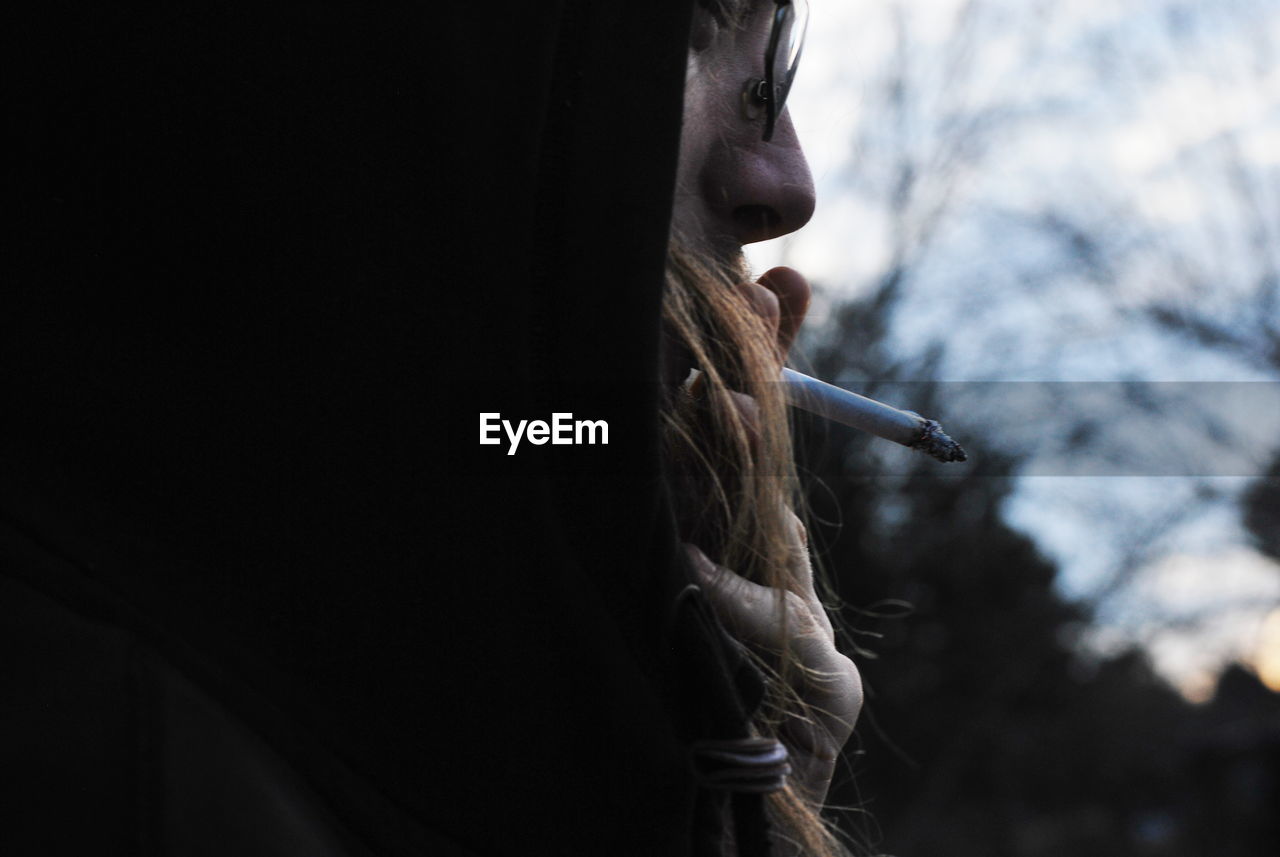 Close-up of man smoking cigarette against sky