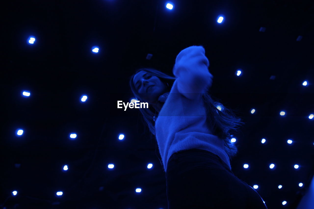 LOW ANGLE VIEW OF ILLUMINATED MAN STANDING AT NIGHT