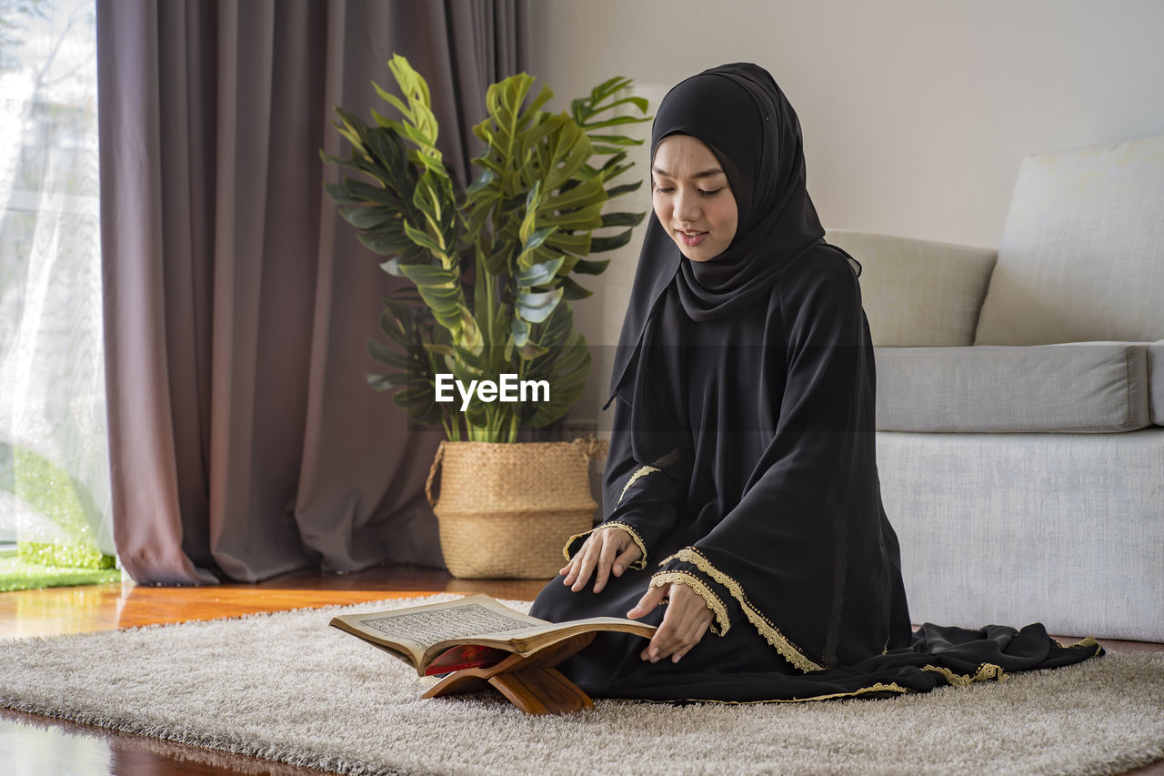 Young woman reading koran while sitting on floor at home