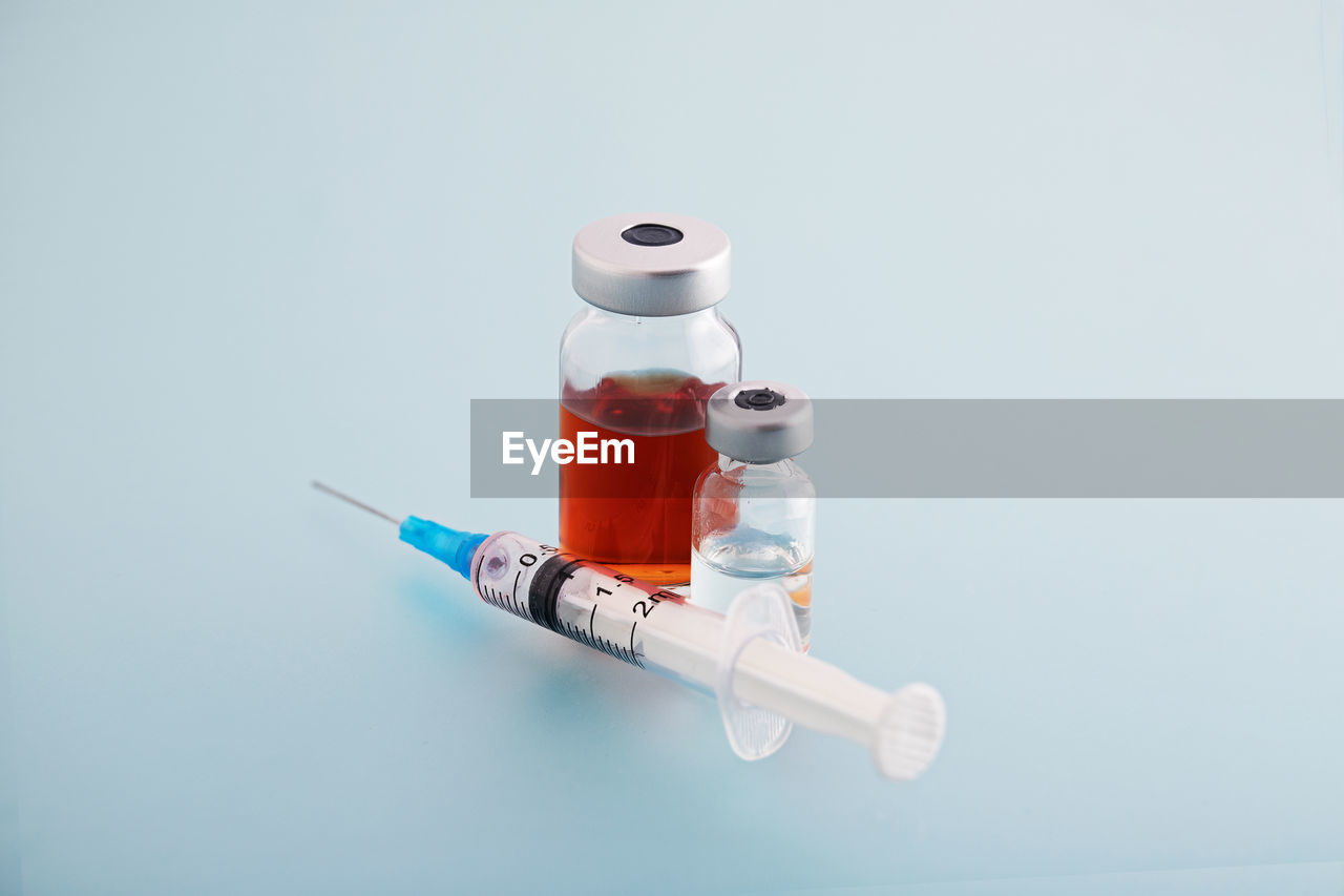 Close-up of syringe with bottles on blue background