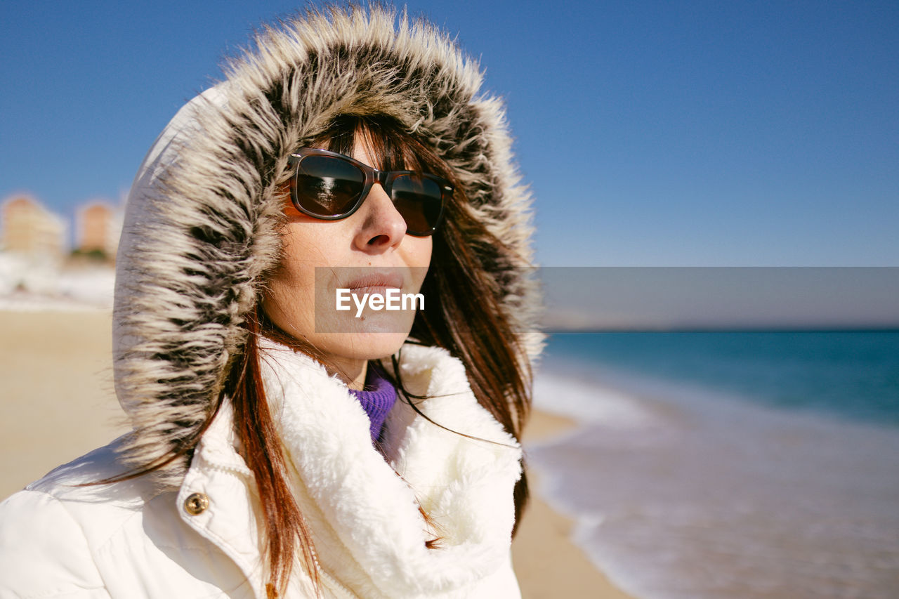 Happy woman in white jacket and sunglasses on a sunny winter day at the beach