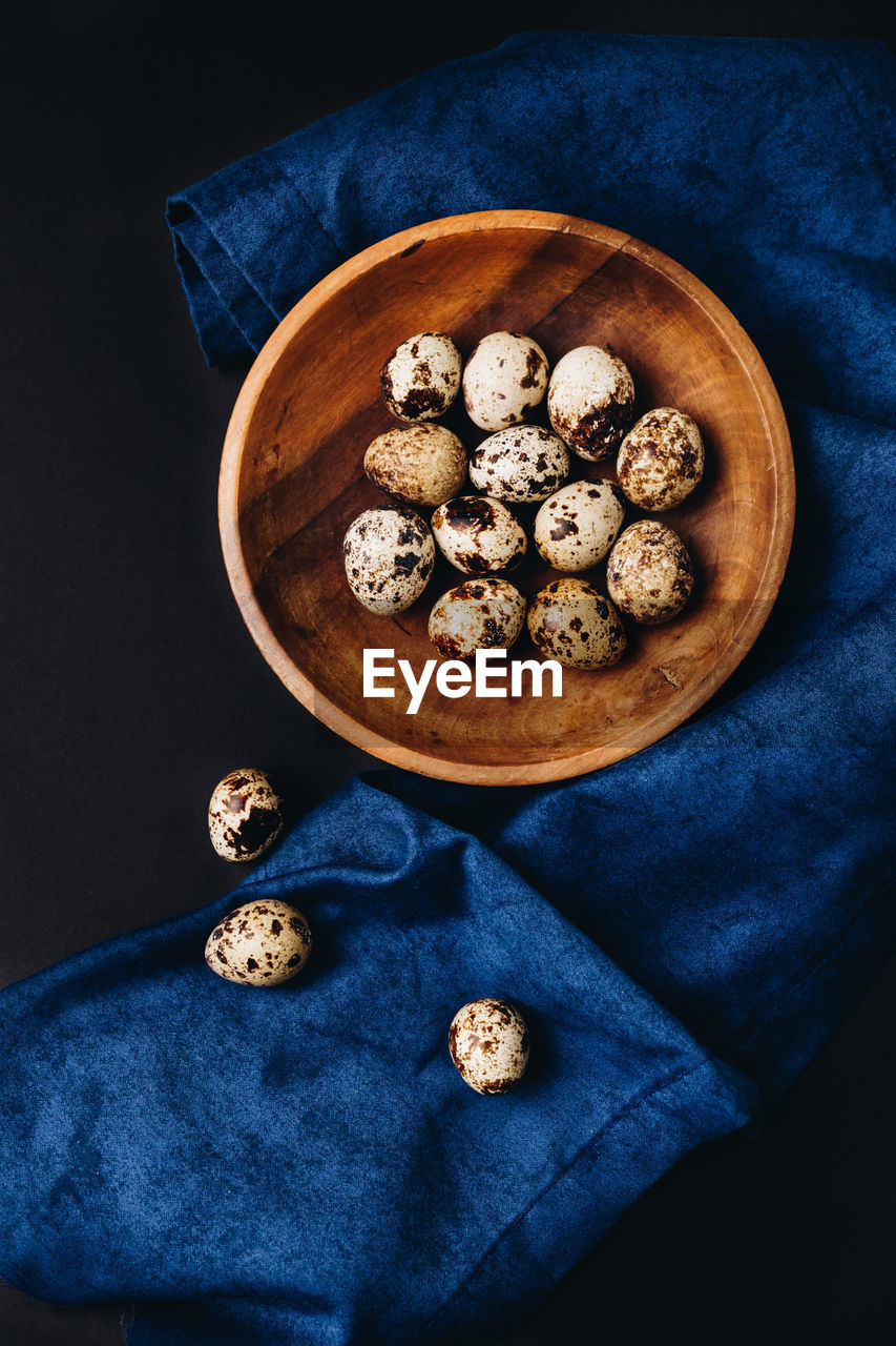 Minimal concept of fresh quail eggs in the wooden bowl on the dark background with blue saten
