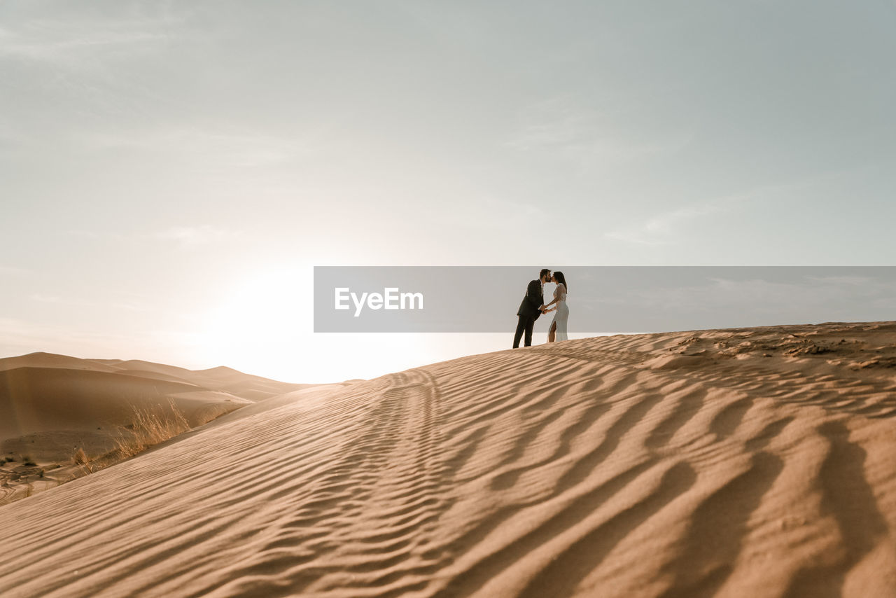 A couple in their wedding clothes on top of a desert dune at dawn. wedding concept