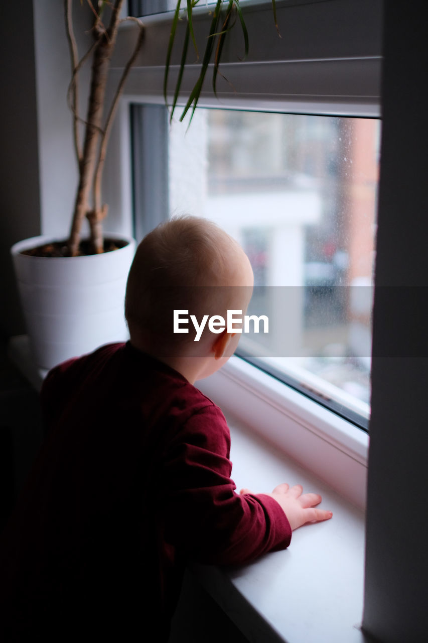 Rear view of toddler  looking out through window at daytime
