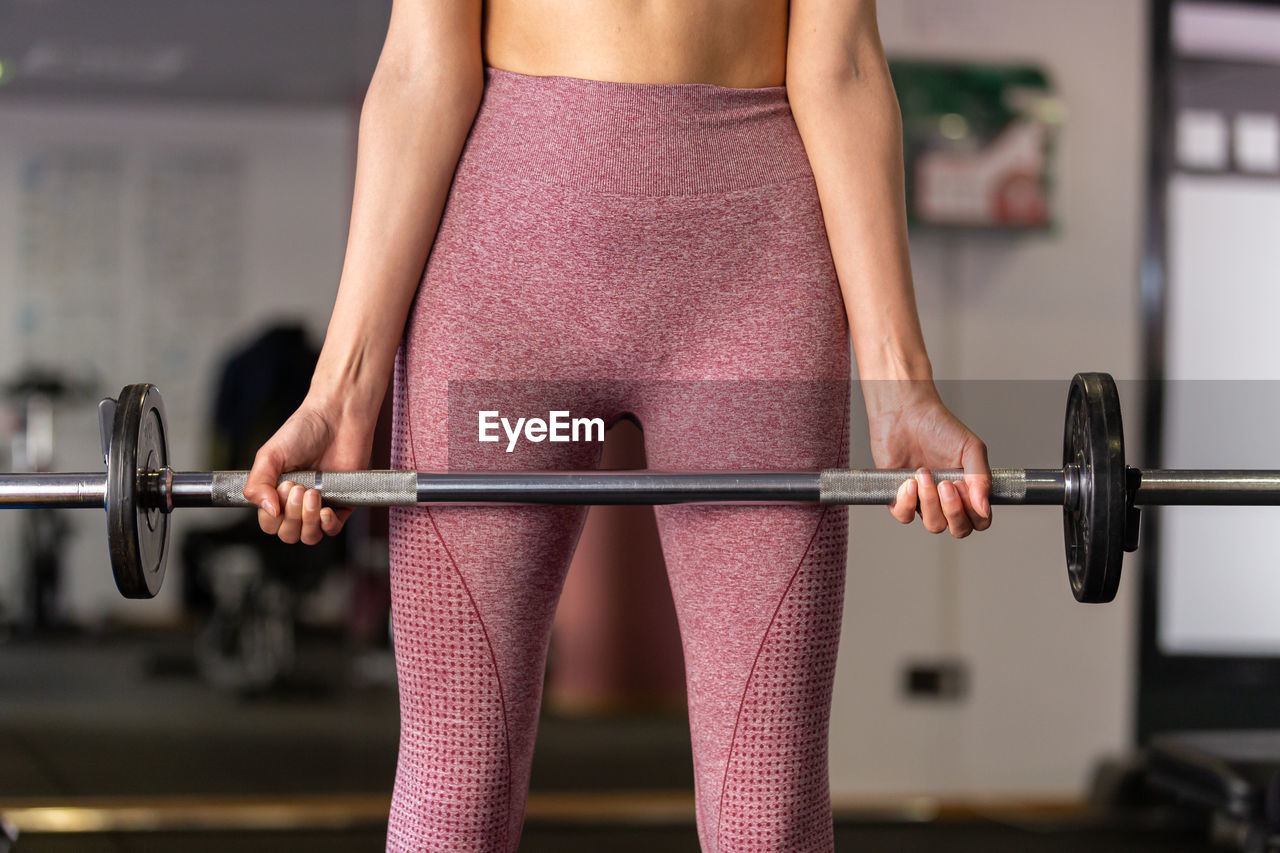 midsection of woman lifting dumbbell in gym