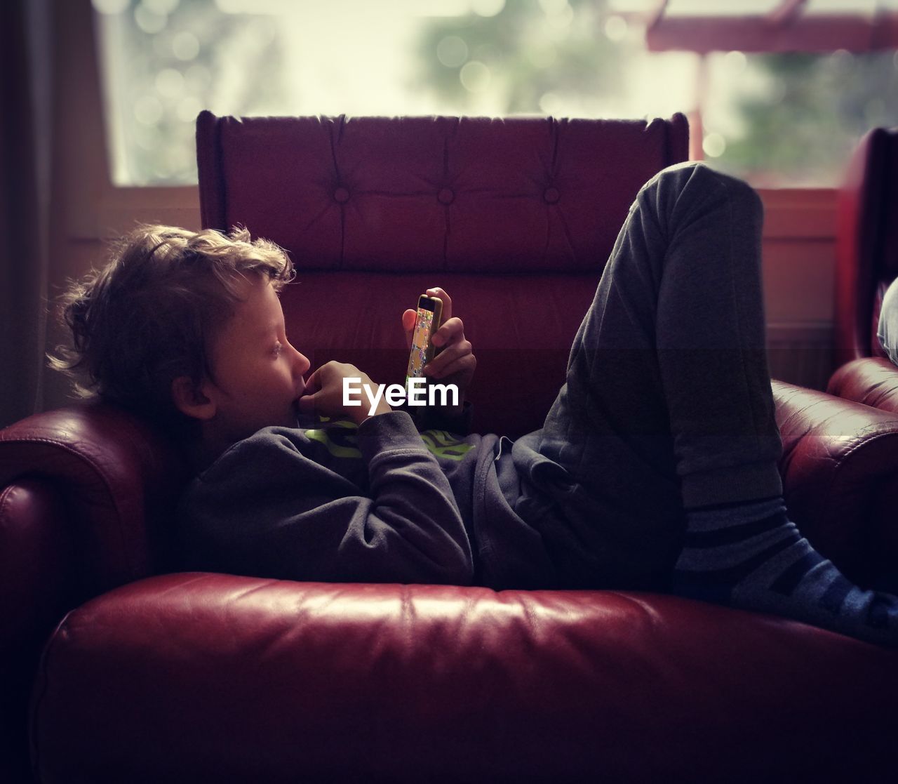 Side view of boy using smart phone while lying on armchair
