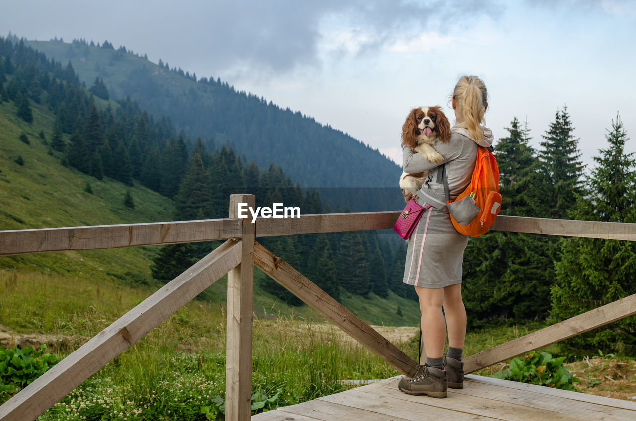 Woman and her dog, cavalier king charles spaniel, on a mountain top, watching a mountain landscape
