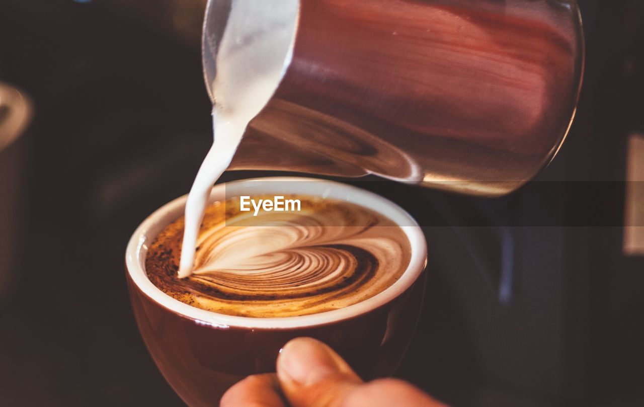 Cropped image of person pouring milk in coffee with heart froth