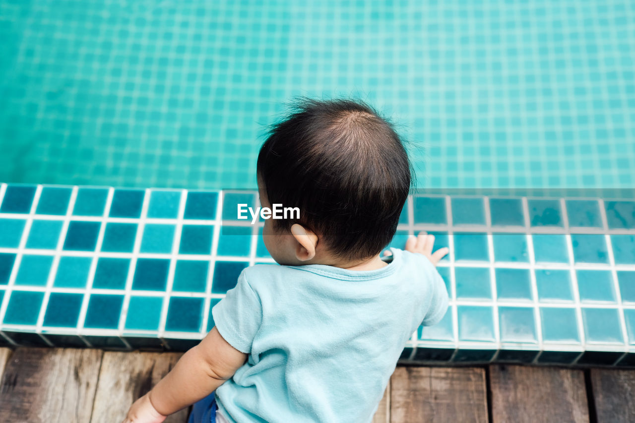 Rear view of baby girl sitting by swimming pool