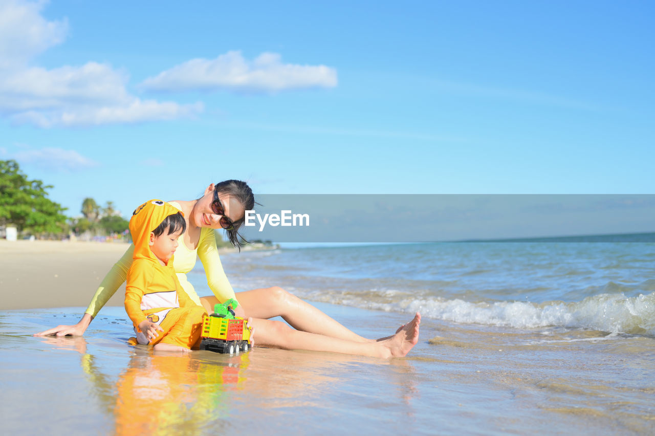 full length of young woman sitting on beach against sky