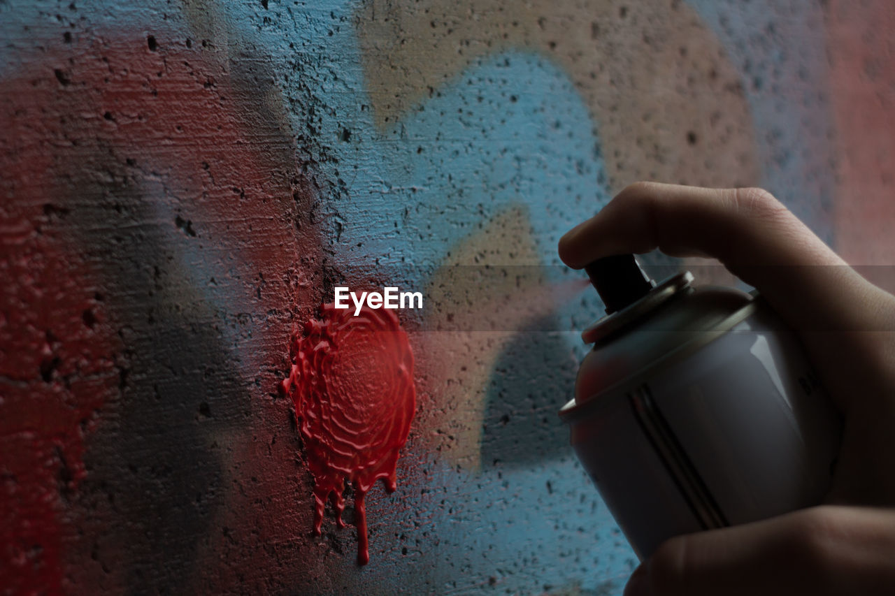Cropped image of hand spraying paint on wall