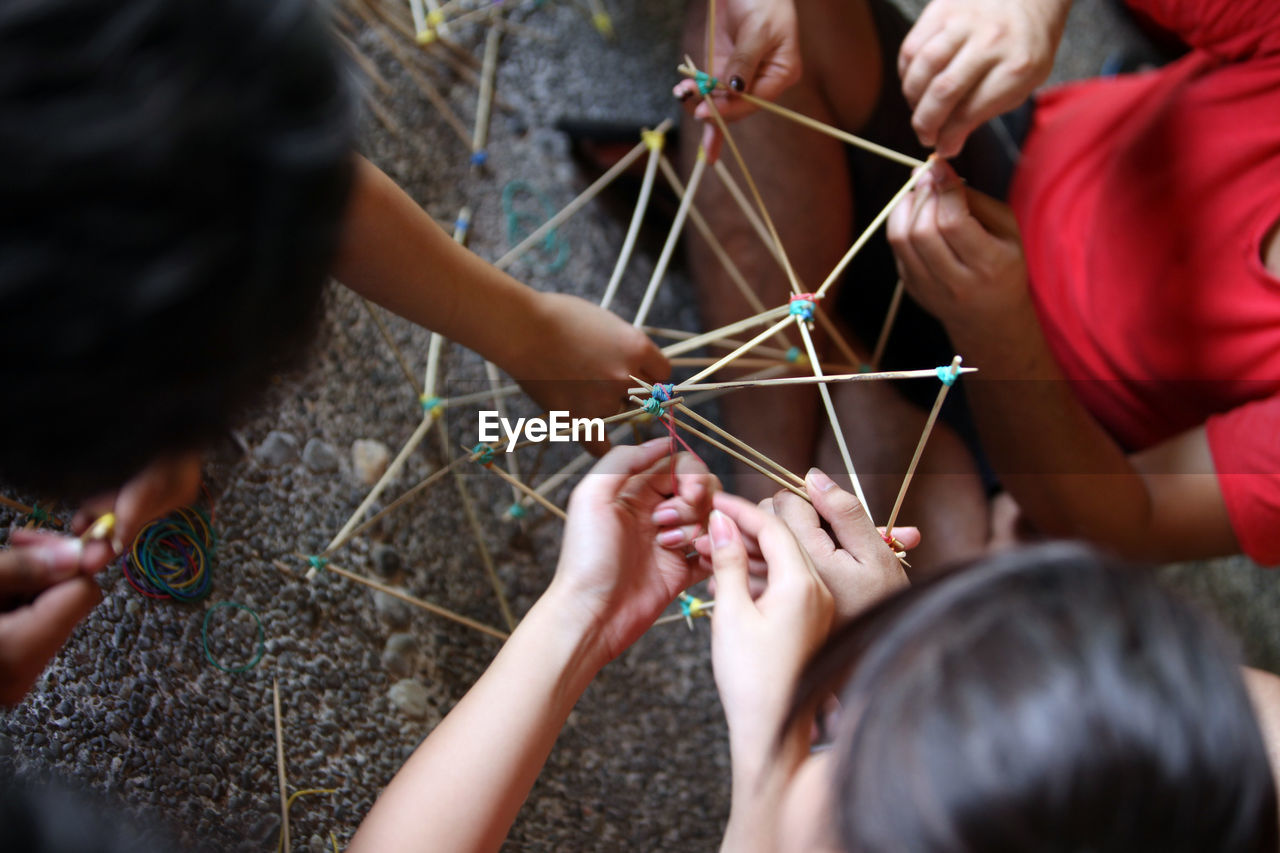 High angle view of friends making model with rubber bands and sticks