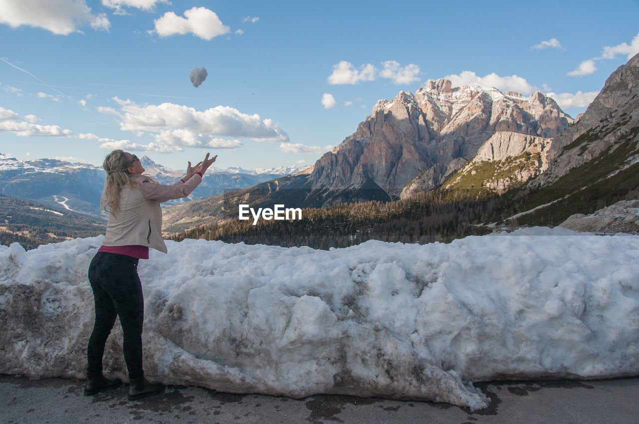 Side view of woman playing with snow on snowcapped mountains against sky