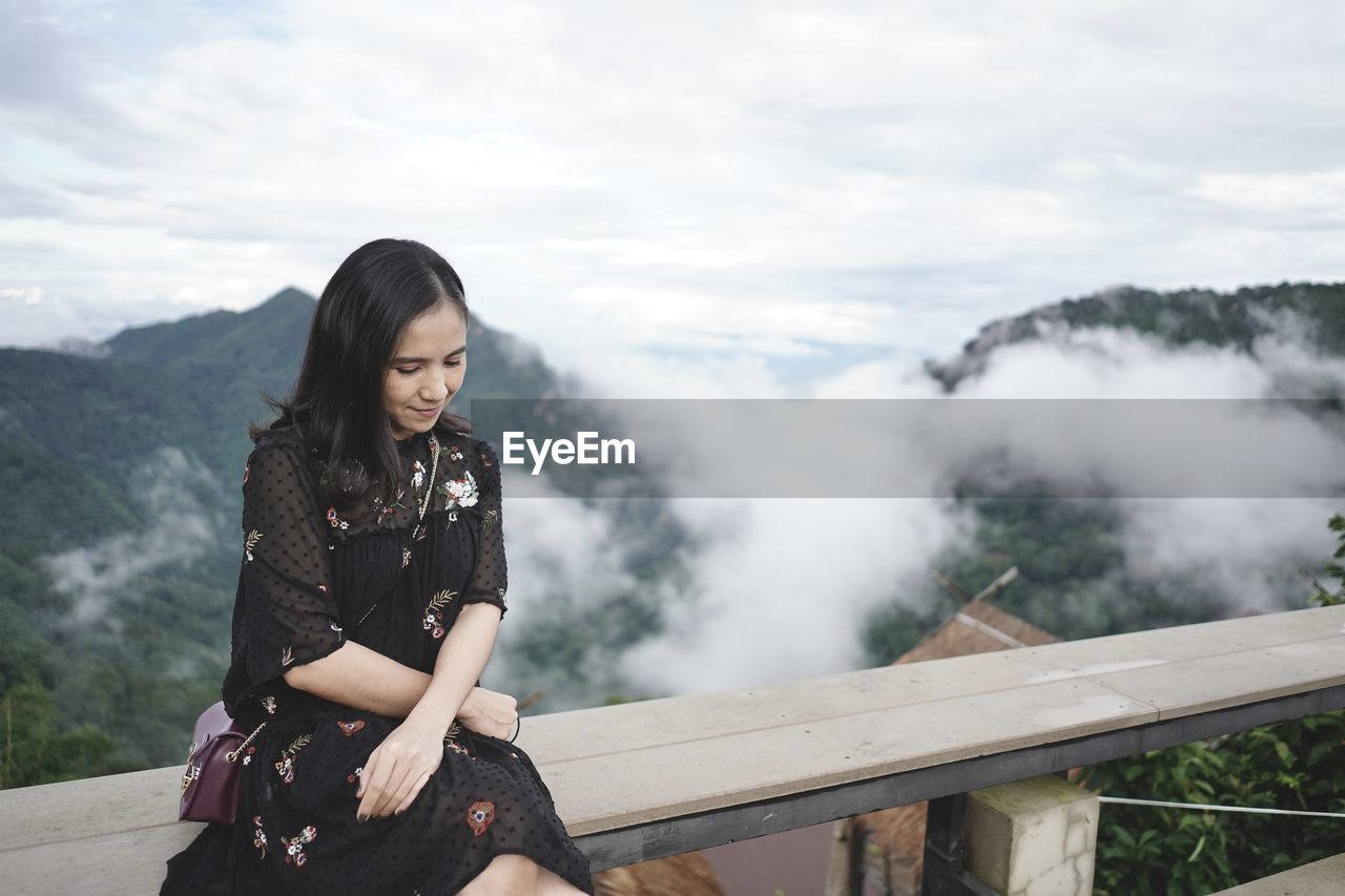Woman sitting on railing against mountain