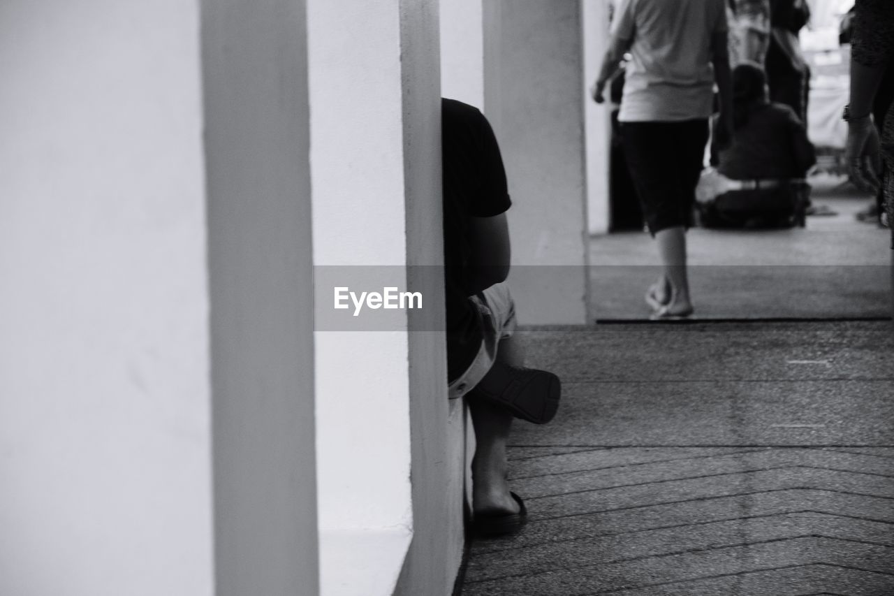 Cropped image of person sitting by wall in corridor