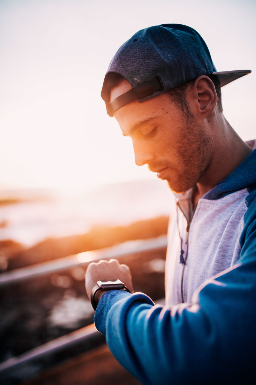 Close-up of man looking at smartwatch at sunset