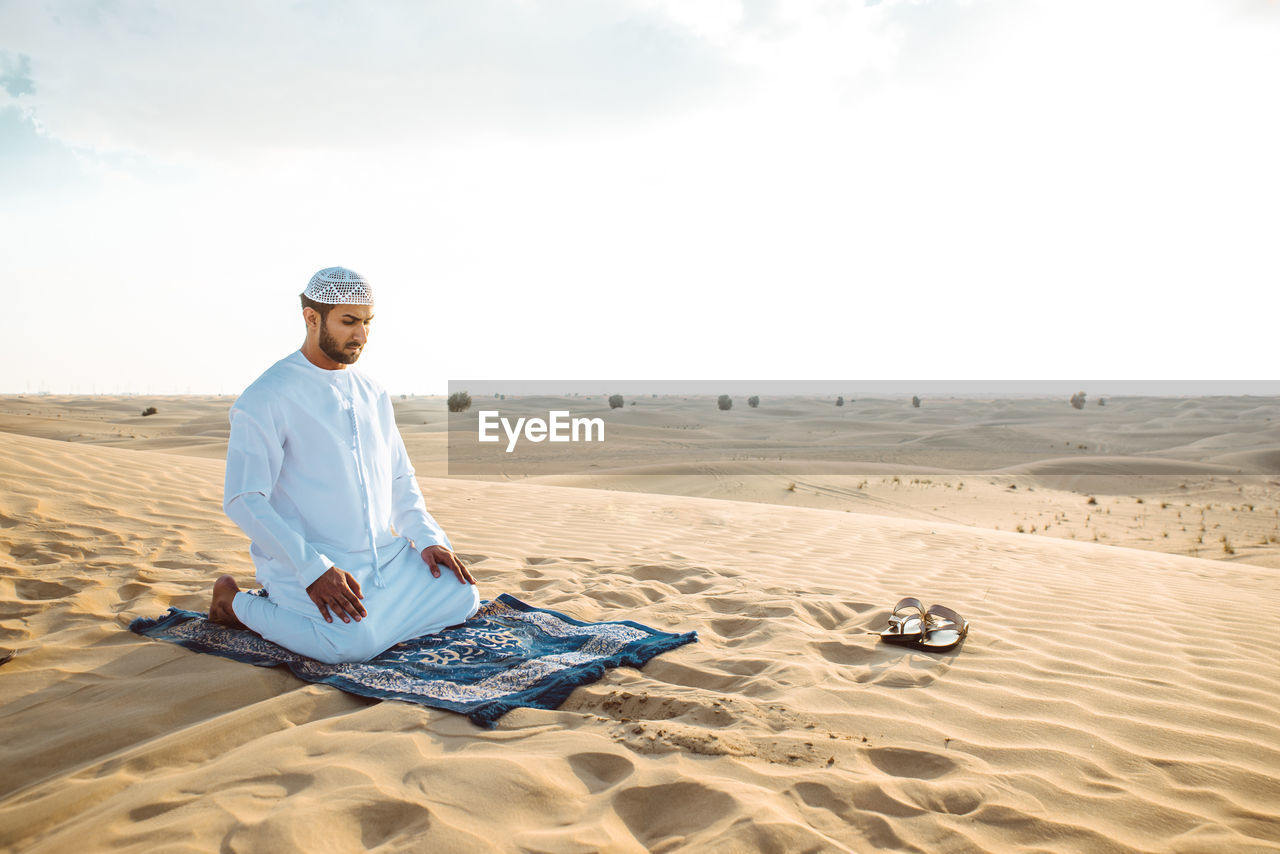 Man praying while sitting on sand in desert