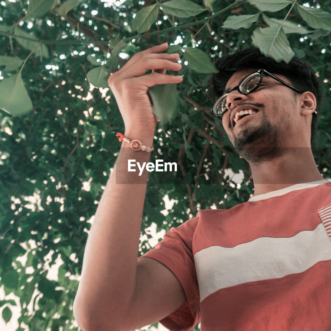 PORTRAIT OF YOUNG MAN HOLDING EYEGLASSES AGAINST PLANTS