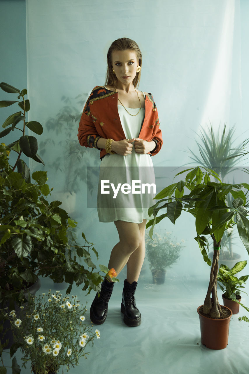 Full length of young woman standing against potted plants