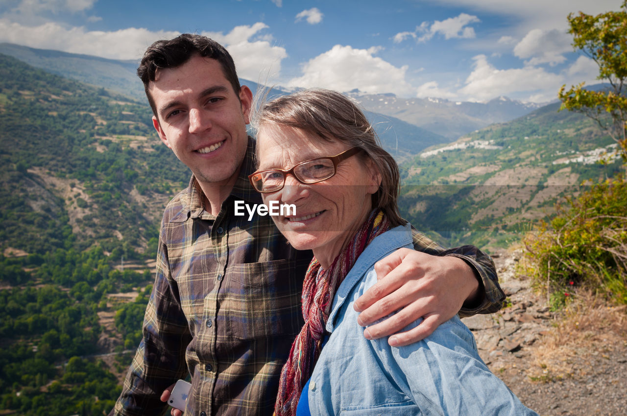 Portrait of young man with senior woman against mountains and sky