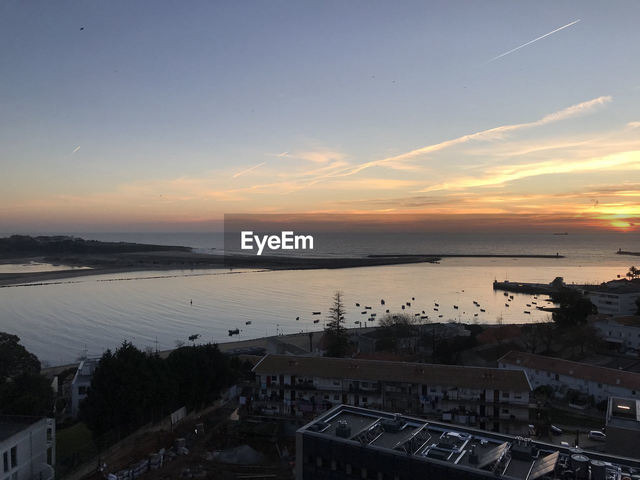 HIGH ANGLE VIEW OF CITY BY SEA AGAINST SKY DURING SUNSET