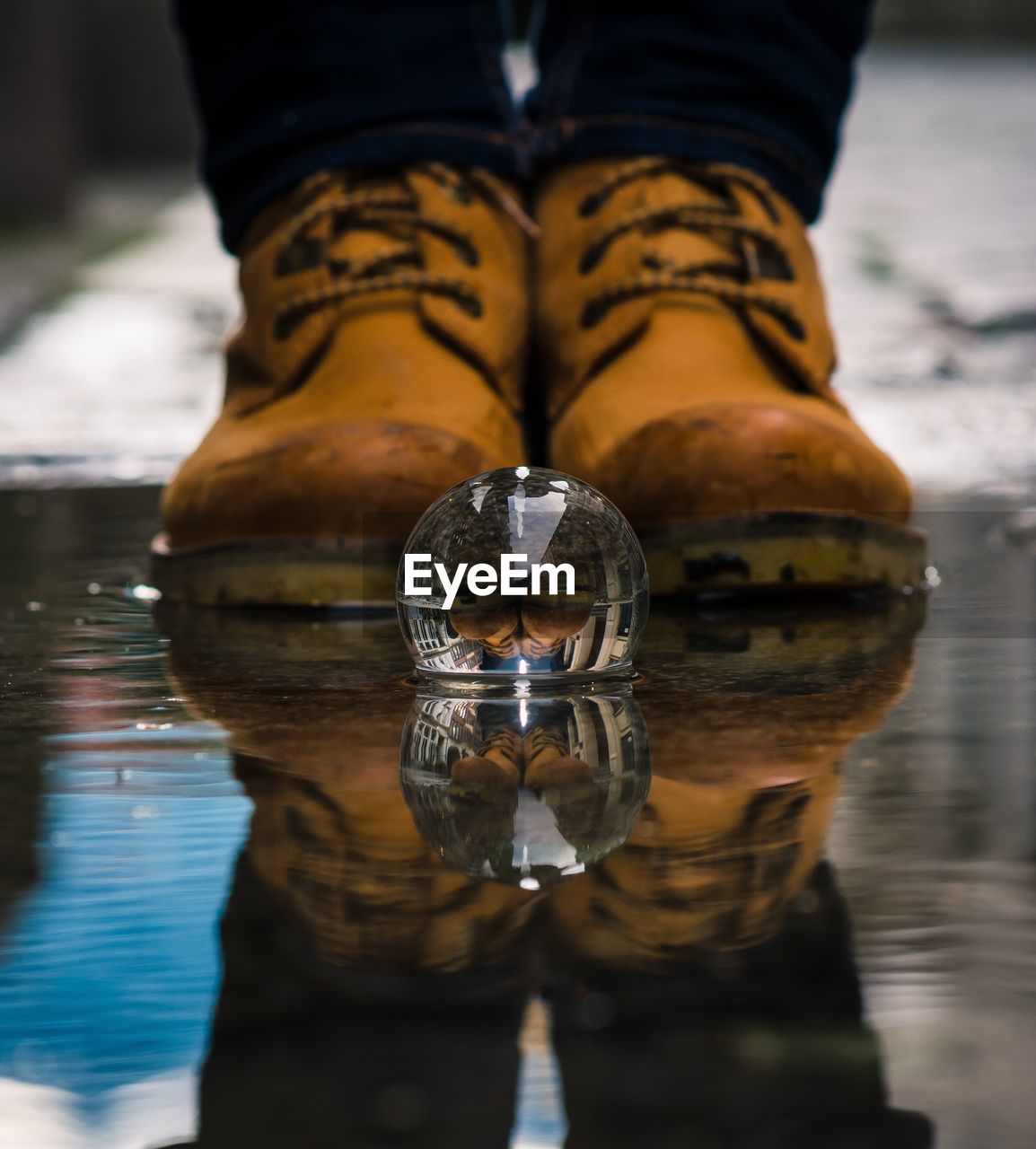 Low section of person reflecting on crystal ball at puddle