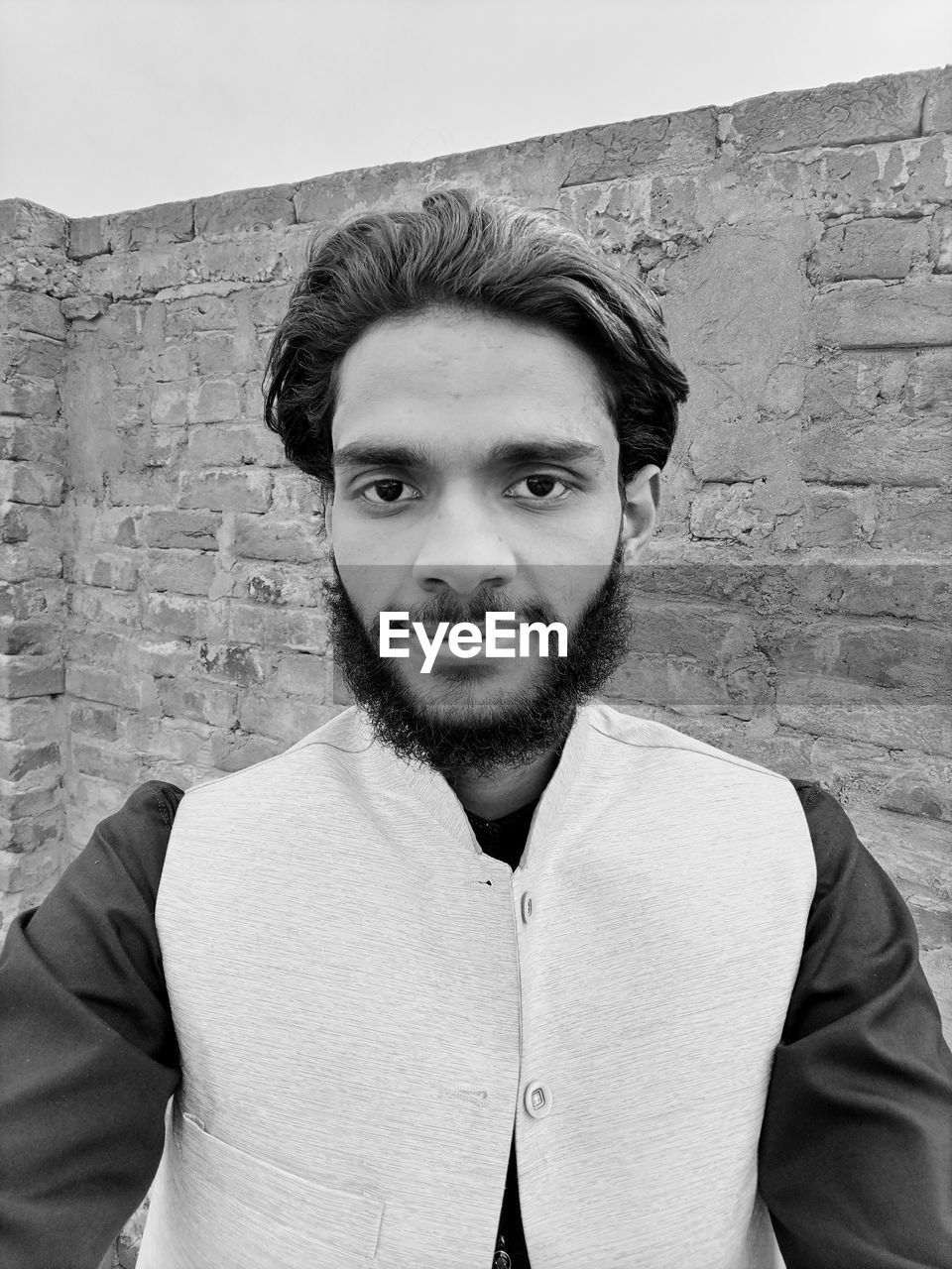 portrait, looking at camera, white, one person, young adult, beard, front view, facial hair, black and white, adult, black, monochrome photography, casual clothing, wall - building feature, men, monochrome, wall, waist up, lifestyles, leisure activity, person, standing, architecture, brick wall, clothing, headshot, smiling, human hair, brick, day, hairstyle, portrait photography, fashion, human face