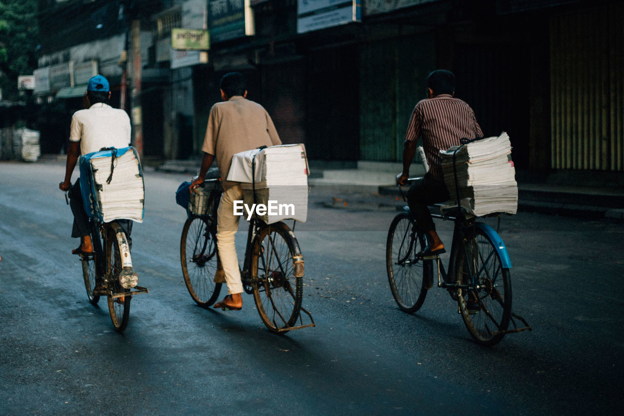 Rear view of newspaper vendors riding bicycles on road in city