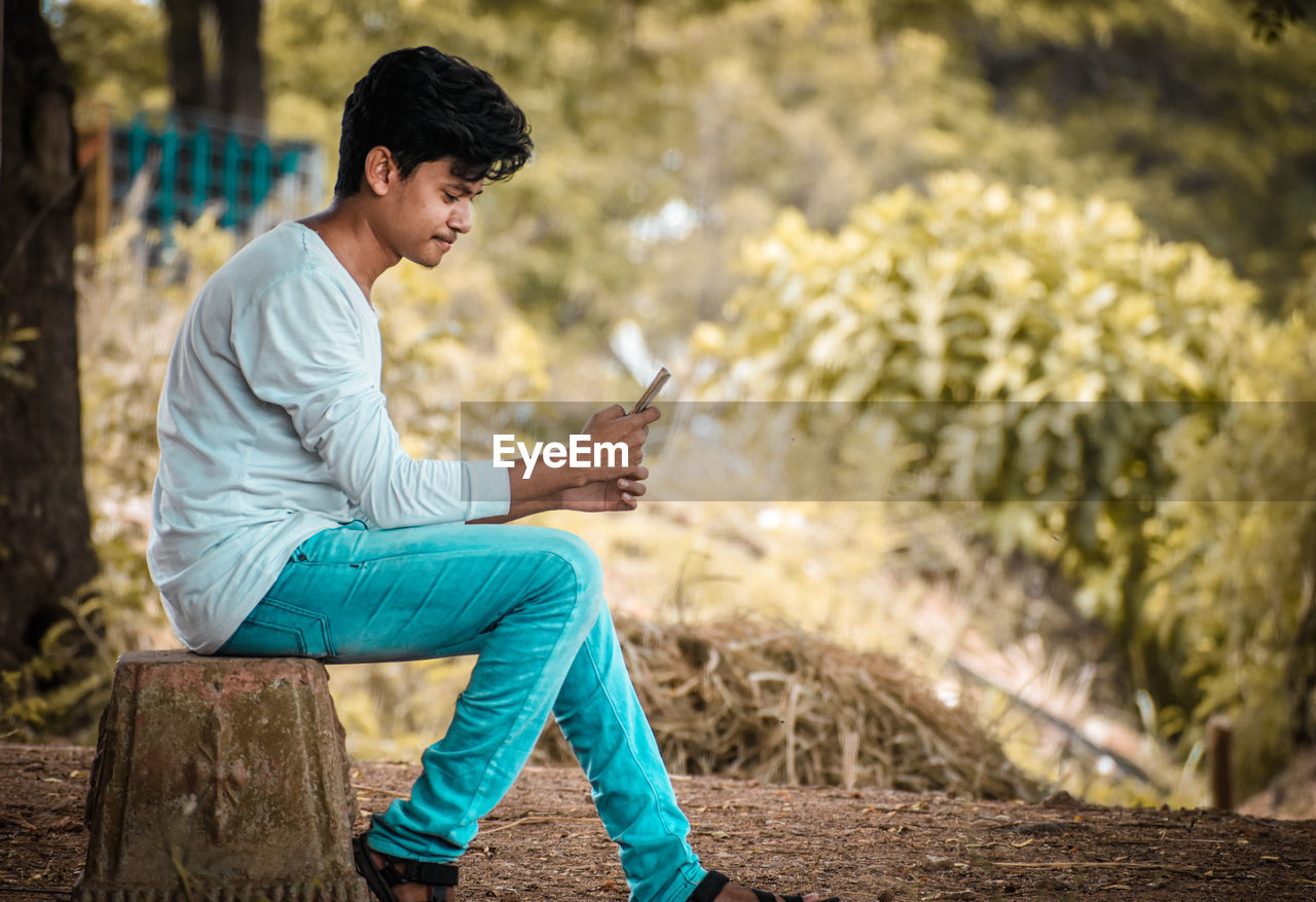 Side view of young man using mobile phone outdoors