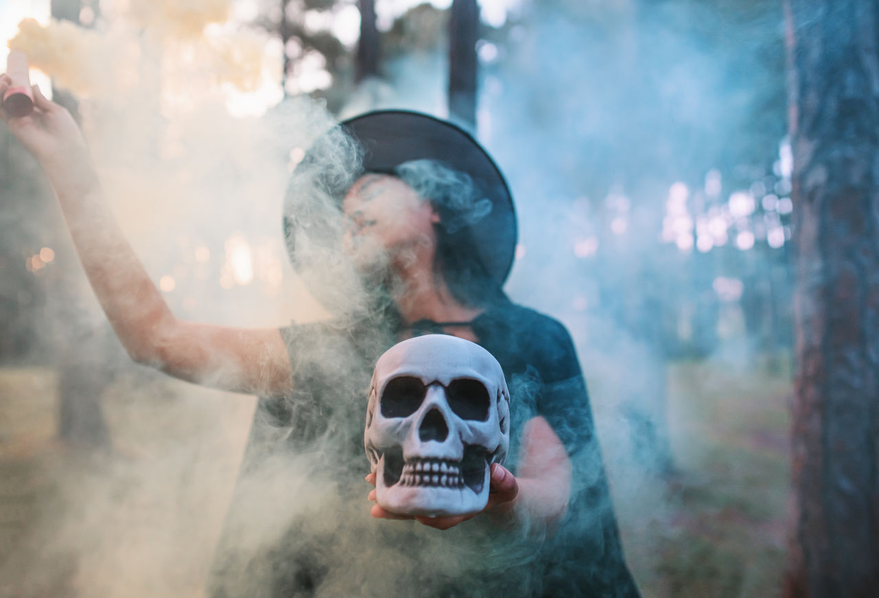 Woman holding distress flare and skull while standing in forest