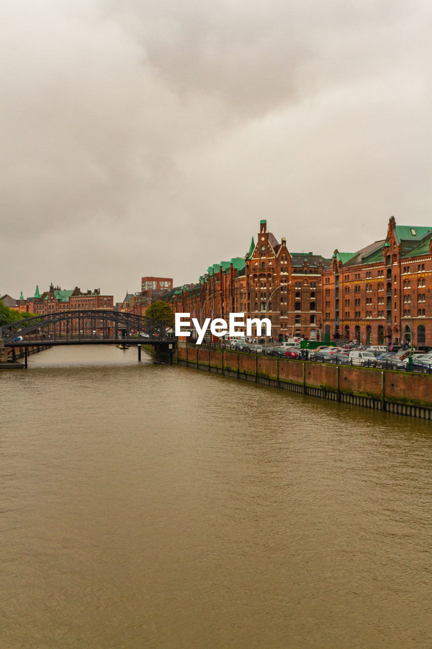 View of buildings at waterfront against cloudy sky