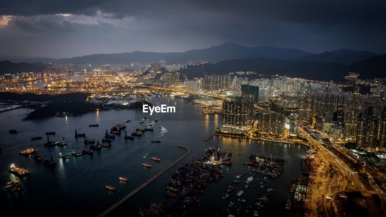 High angle view of victoria harbour by illuminated cityscape at night