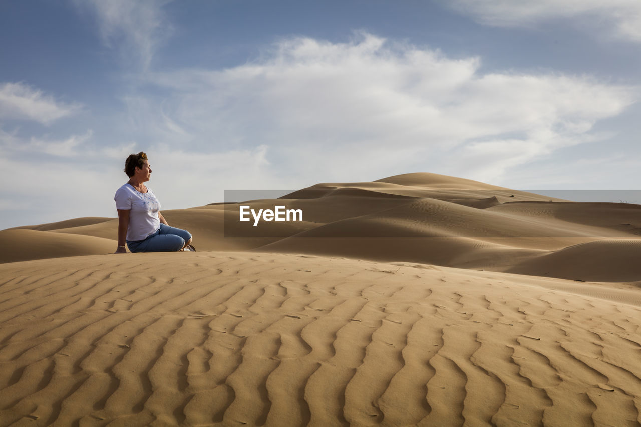 FULL LENGTH OF MAN SITTING ON SAND DUNE IN DESERT